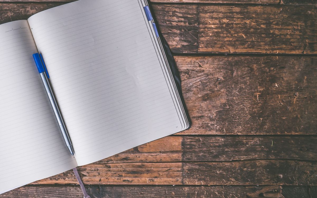 An open blank notebook and a pen on a worn wooden table