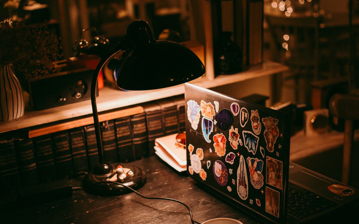 A home desk with a lamp, a laptop and a row of books, lit at night