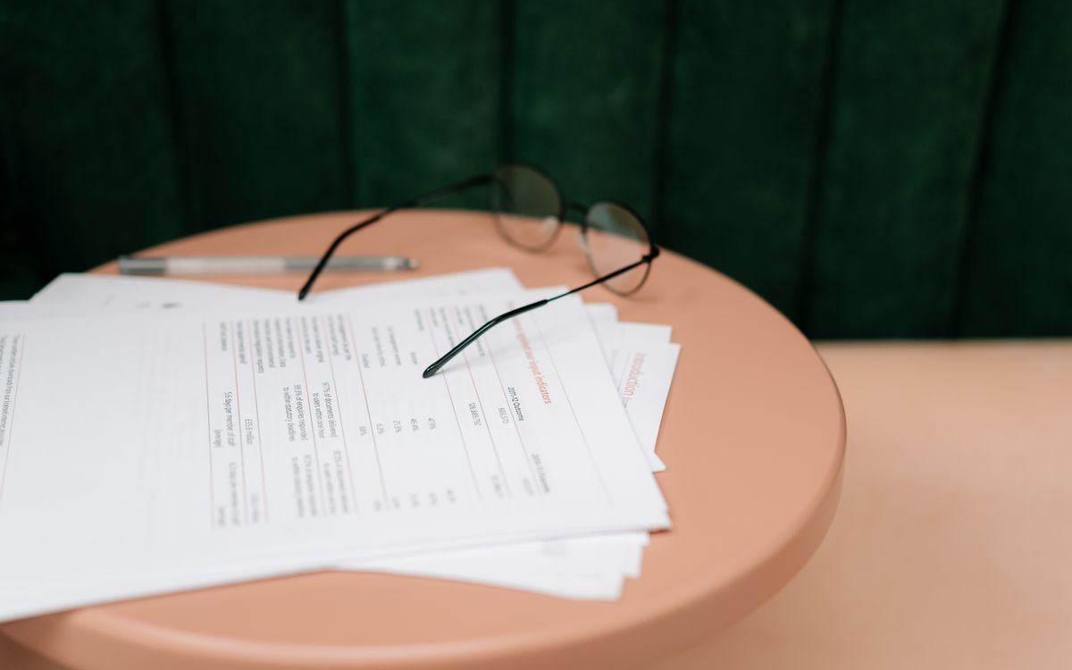 A stack of documents, a pen and reading glasses on a round table