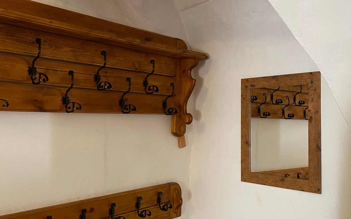 An empty wooden coat rack on a white wall beside a small mirror