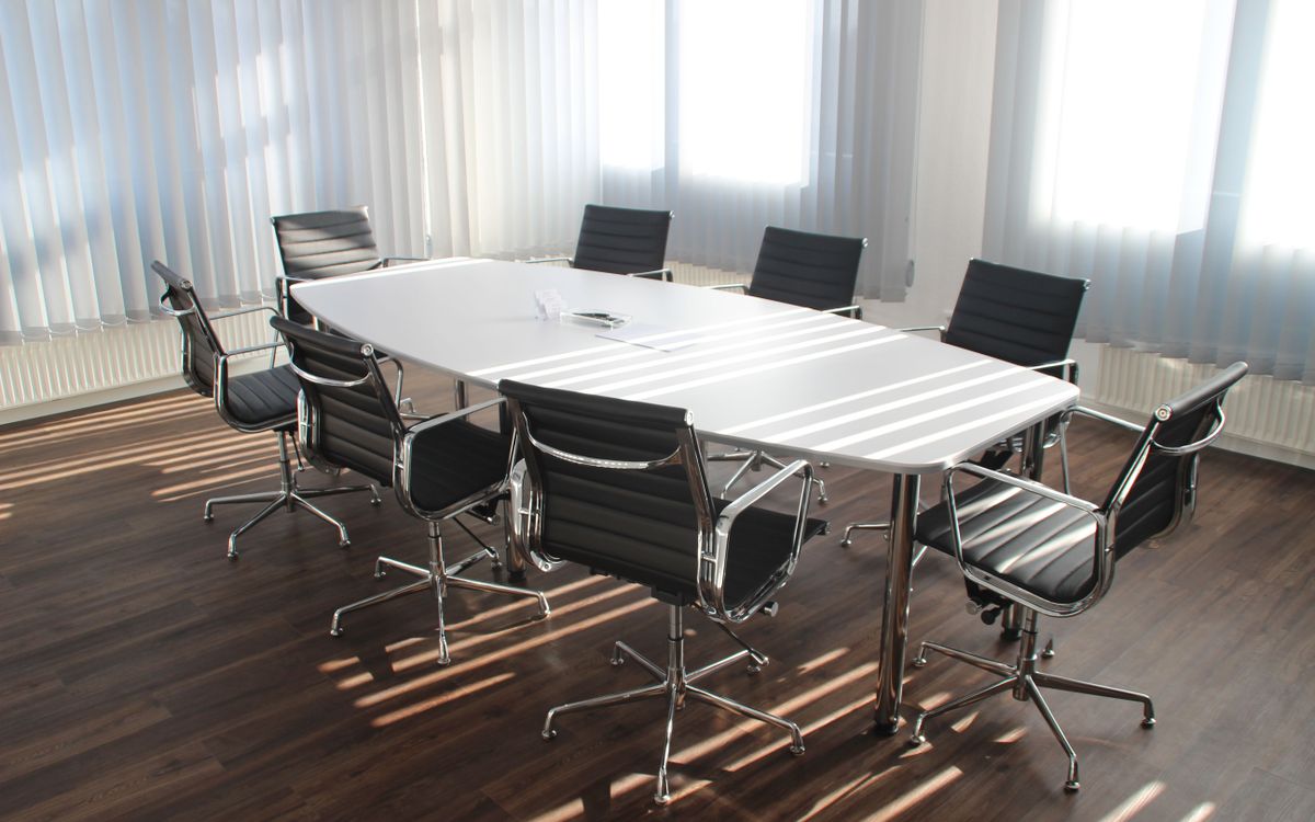 An empty meeting room with a white table and chairs, sunlight through blinds