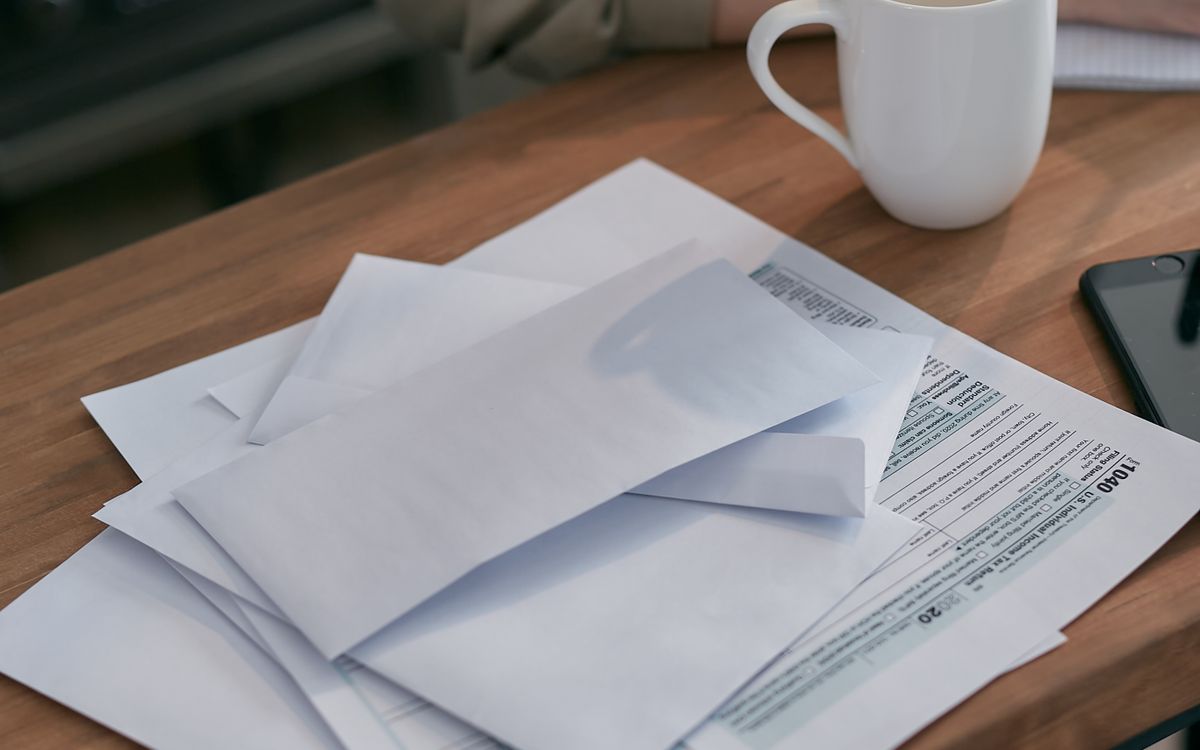 Unopened envelopes and a tax form on a wooden kitchen table beside a mug