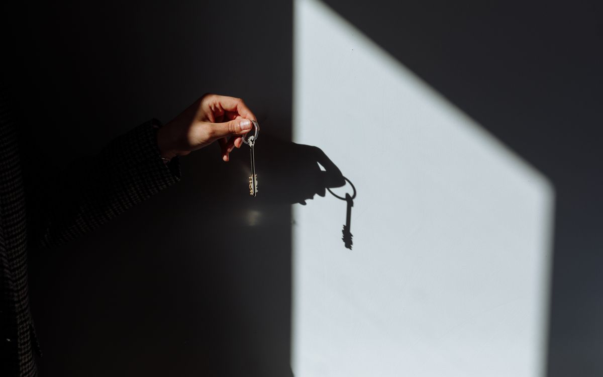 A hand holding out a door key, its shadow cast on a sunlit wall