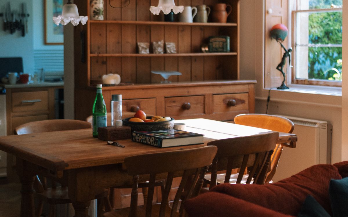 A lived-in wooden kitchen table with chairs, in afternoon light