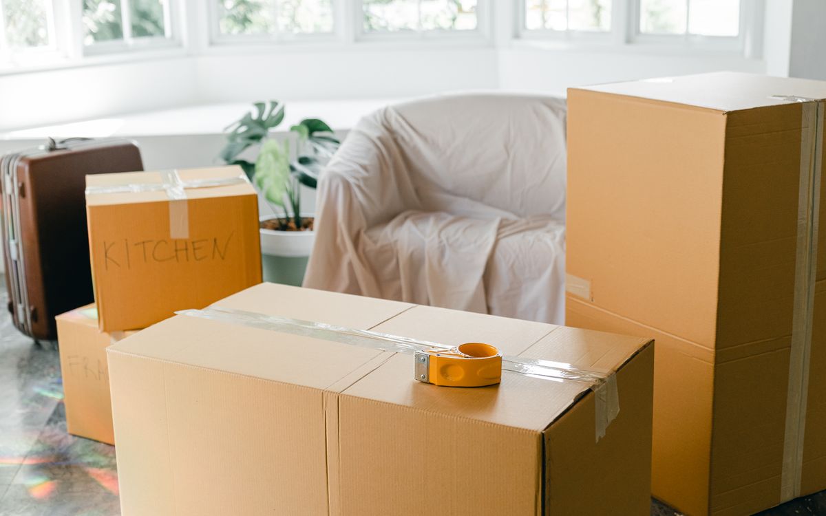 Labeled cardboard boxes and a sheeted armchair in a bright, half-packed room