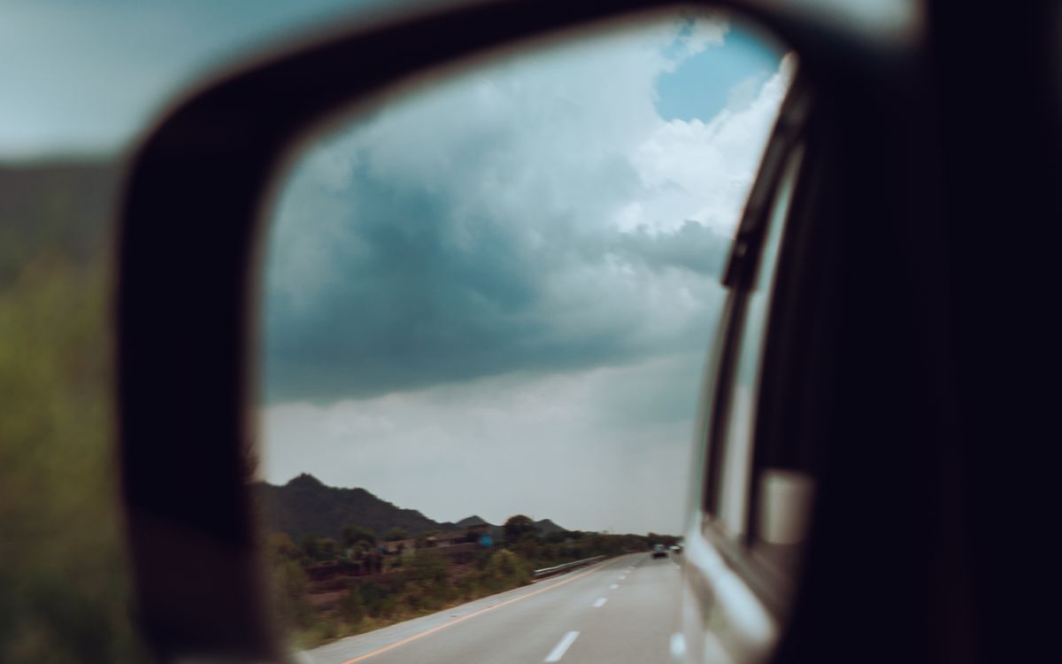 A highway and cloudy sky reflected in a car side mirror