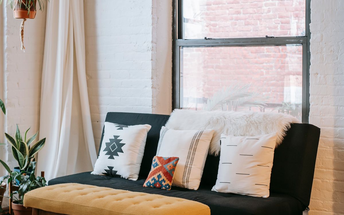 A sofa with mismatched cushions beside a window in a brick-walled room
