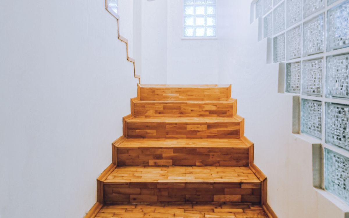 An empty wooden staircase in a house lit by daylight through glass block windows