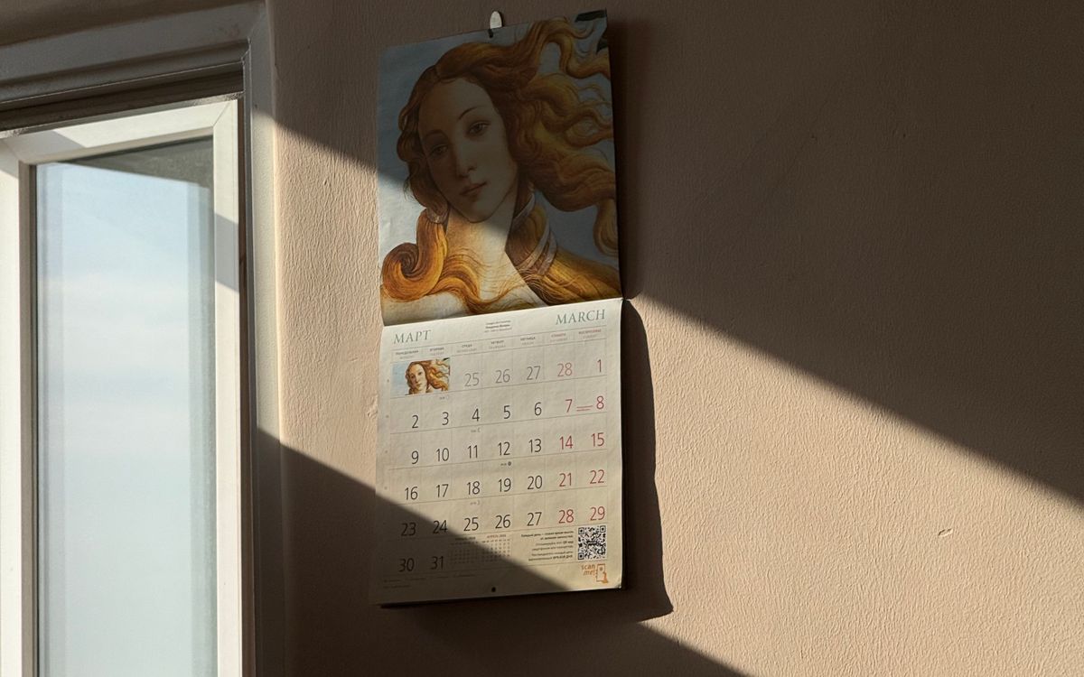 A wall calendar beside a window with afternoon light across the wall