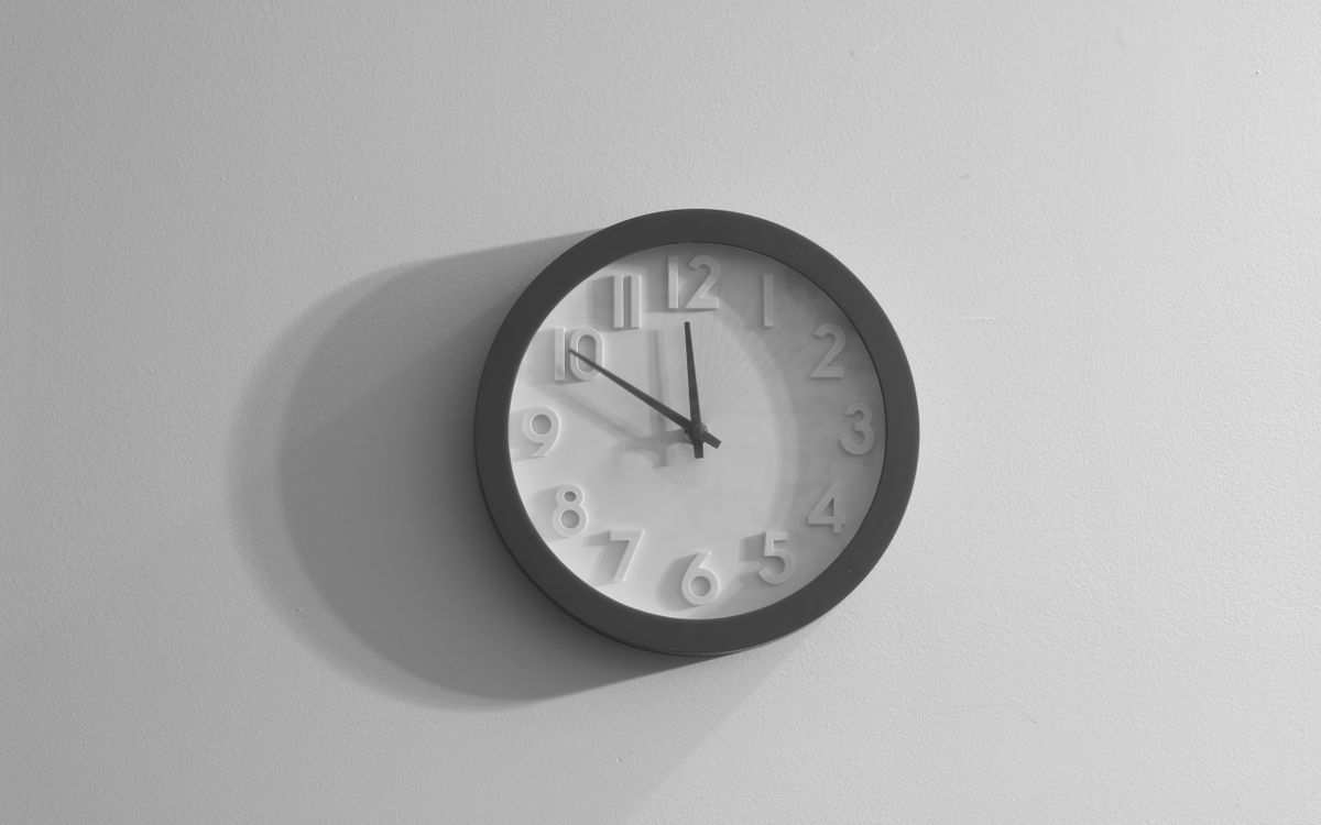 A plain wall clock casting a soft shadow on a white wall